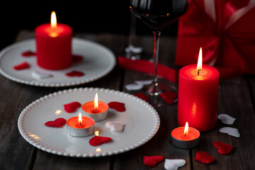 Saint Valentine's Day celebration. Red burning candles, hearts, gift box, postcard on dark wooden background. Happy holiday . Table decor for festive dinner, romantic atmosphere