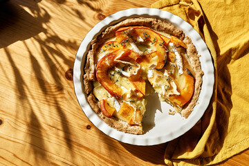 Autumn healthy eating. Delicious seasonal tart with baked pumpkin, brie cheese and herbs on wooden table.