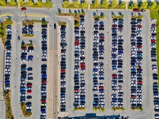 An aerial top view of a vast parking lot with rows of parked cars
