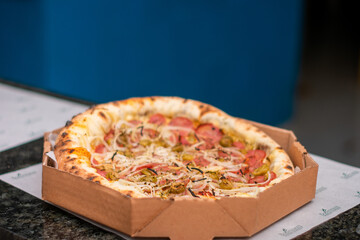 Brazilian pizza, pepperoni pizza with cheese, tomato sauce, cheese, onion rustic wooden background and delivery box