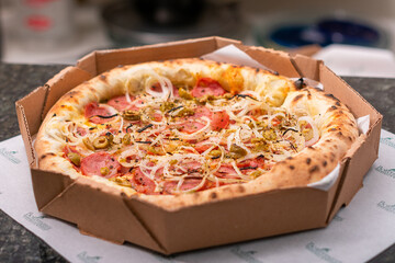 Brazilian pizza, pepperoni pizza with cheese, tomato sauce, cheese, onion rustic wooden background and delivery box