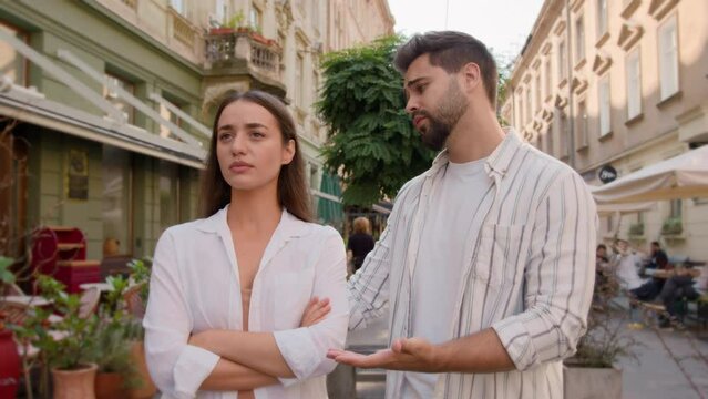 Young couple city annoyed offended angry woman arms crossed guilty man apologize quarrel outside street discomfort emotions feel disagreement crisis relationship problems ignore together regret sorry