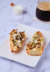 Sandwiches on a baguette with hummus, oyster mushrooms and parmesan cheese on a white ceramic plate on a marble background. Modern style in food photography, minimalism.