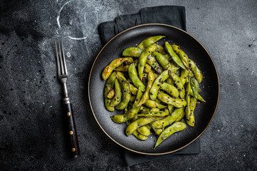 Stir-fried green Edamame Soy Beans with sea salt and sesame seeds in a plate. Black background. Top...
