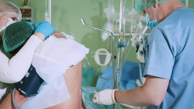 Male doctor injecting Epidural Anesthesia for pregnancy Labor during childbirth for women patient in hospital. Preparing the final stages before surgery. Shot of a woman sitting on her hospital bed.
