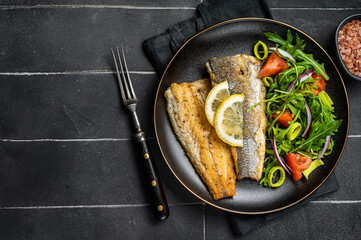 Roasted sea bass fillet with salad, Branzino fish. Black background. Top view. Copy space - obrazy, fototapety, plakaty