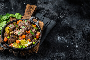 Beef stew with potato, carrot and herbs in a skillet. Black background. Top view. Copy space