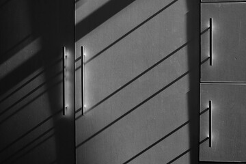 Metal door in a wall with shadows cast from the window nearby, grayscale view