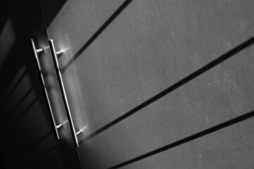 Metal door in a wall with shadows cast from the window nearby, grayscale view