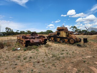 a couple of rusty tanks on the dirt ground near trees