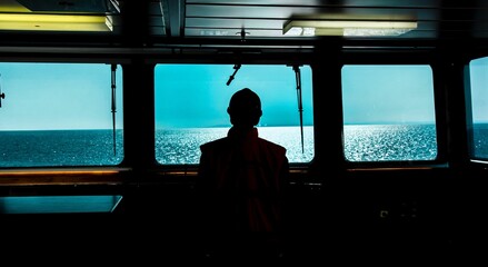 Silhouette of the captain standing near the window on a ship, taking in the view as the vessel sails - obrazy, fototapety, plakaty