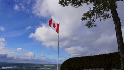 Fototapeta premium Canadian flag near the beach with cloudy blue sky in the background