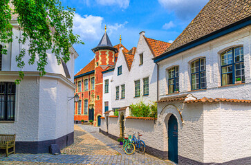 Beguinage Courtrai of Saint-Elisabeth, Begijnhof van Kortrijk with white houses and Sint-Annazaal museum, bicycles near wall on narrow cobblestone street in Kortrijk city historical centre, Belgium - obrazy, fototapety, plakaty