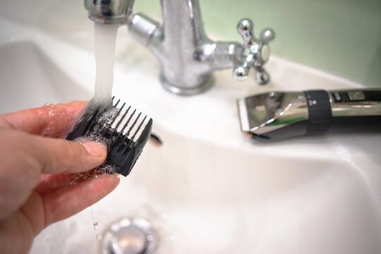 Cleaning the attachments for the hair clipper. Wash the electric clipper under the tap.