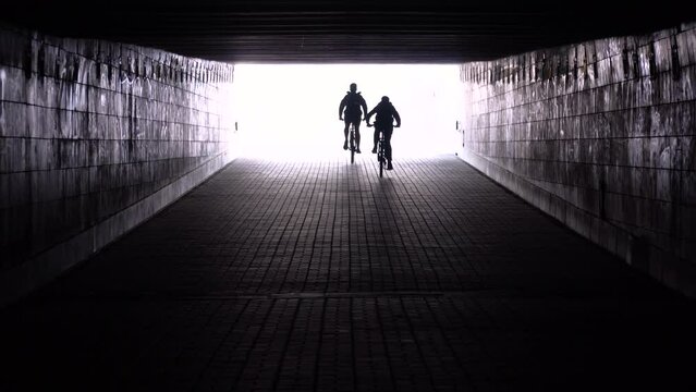 two bicycle riders are moving away through an underground passage 