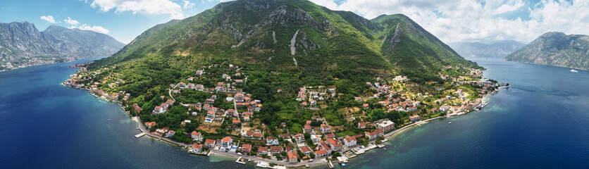 Old houses with red roofs on the seashore on the slope of a green mountain. Montenegro. Drone....