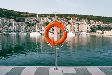 Orange lifebuoy on a stand on a pier against the backdrop of a colorful resort town with moored...