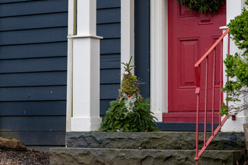 A Christmas gnome decoration on the step of a blue house with a vibrant red door, white columns,...