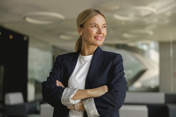 Portrait of smiling female entrepreneur with crossed hands standing in office and looks away