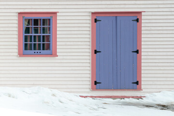 The exterior wall of a white wooden cape cod clapboard siding house with a purple panel door and...