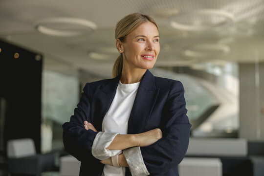 Portrait of smiling female entrepreneur with crossed hands standing in office and looks away