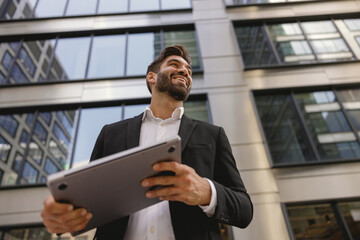 Stylish male manager with laptop standig on office terrace and looks away. High quality photo