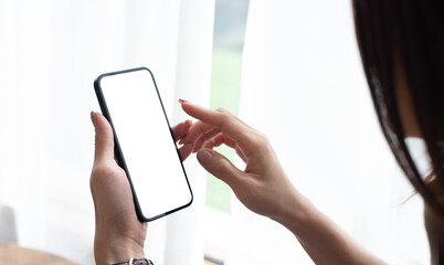 Young woman hands holding cell phone touching finger on mockup white blank display, empty screen for social media app ad at home. Mobile application tech concept, over shoulder view, closeup