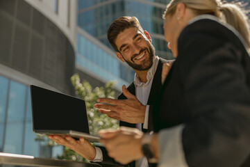 Two business people discuss biz issue while use laptop standing on modern office terrace