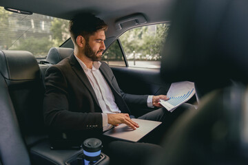 Confidence businessman sitting on car backseat and working with documents and use laptop