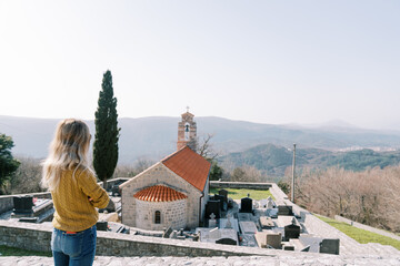 Young woman looks at the church of St. Nicholas and the cemetery around it. Baosici, Montenegro....
