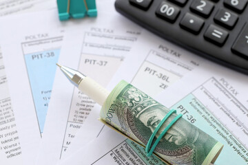 Declaration of the amount of earned income or incurred loss, PIT-36, PIT-36L, PIT-37 and PIT-38 tax forms on accountant table with pen and polish zloty money bills close up