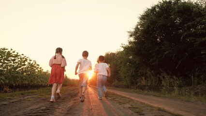 Little boys and girl run playing together along road at sunset countryside