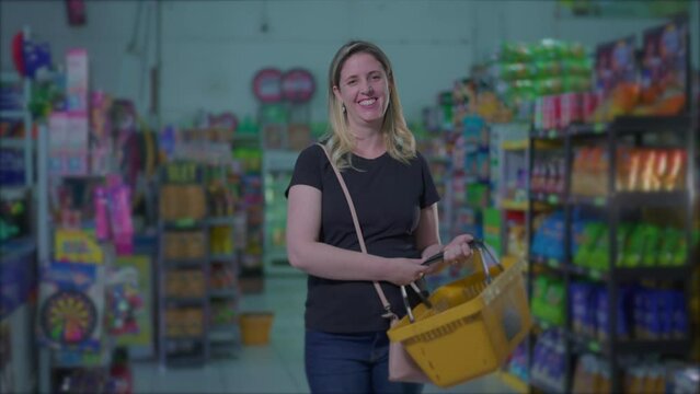 Female consumer smiling while standing inside Supermarket store holding basket, casual authentic real life people depicting consumerism lifestyle habits