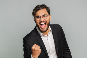 Happy joyful Indian businessman celebrating success victory, winning birthday, lottery jackpot goal achievement play game good positive news, triumph. Young Arabian man isolated on gray background