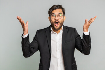 Excited amazed Indian young businessman touching head and showing explosion, looking worried shocked, inspiration, brainstorm, success. Male Arabian man guy in formal suit isolated on gray background