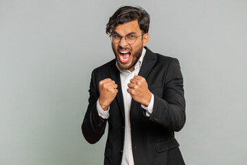 Aggressive angry Indian businessman trying to fight at camera, shaking fist, boxing with expression, punishment, threaten, bullying, abuse, mad fury. Arabian man guy isolated on gray studio background