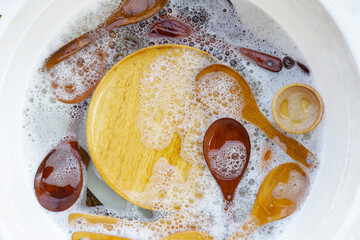 Wooden kitchenware in water and bubbles of dishwashing liquid