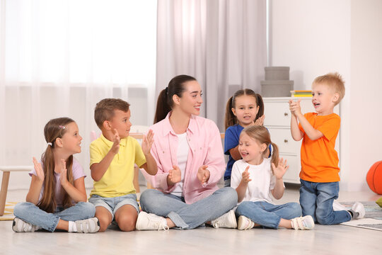Nursery teacher and group of cute little children spending time together on floor in kindergarten. Playtime activities - Powered by Adobe