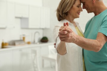 Happy senior couple dancing in kitchen, focus on hands - Powered by Adobe