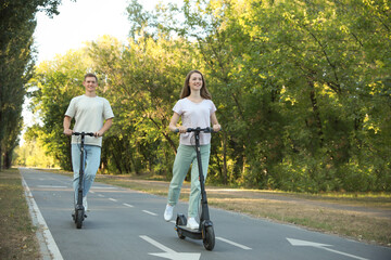 Happy couple riding modern electric kick scooters in park