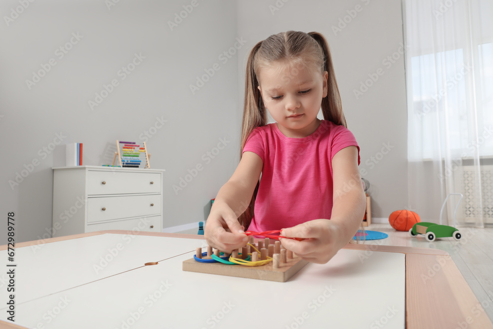 Wall mural Motor skills development. Girl playing with geoboard and rubber bands at white table in kindergarten. Space for text