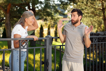 Emotional neighbours having argument near fence outdoors