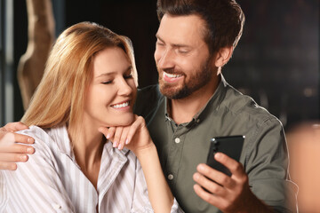 Romantic date. Happy couple with smartphone spending time together indoors