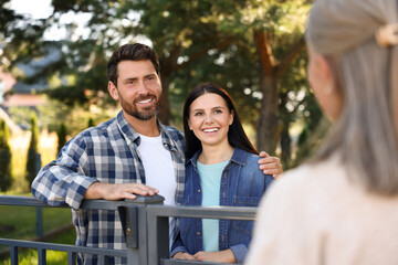 Friendly relationship with neighbours. Happy young couple and senior woman near fence outdoors
