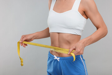 Slim woman measuring waist with tape on grey background, closeup. Weight loss