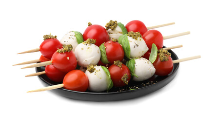 Plate of Caprese skewers with tomatoes, mozzarella balls, basil and pesto sauce isolated on white