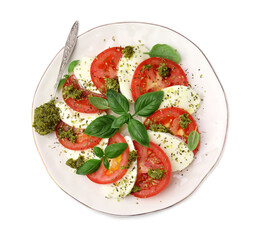 Plate of delicious Caprese salad and spoon with pesto sauce isolated on white, top view
