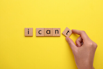 Motivation concept. Woman changing phrase from I Can't into I Can by removing wooden square with letter T on yellow background, top view - obrazy, fototapety, plakaty