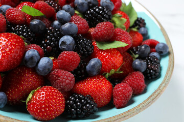 Many different fresh ripe berries in bowl on white table, closeup