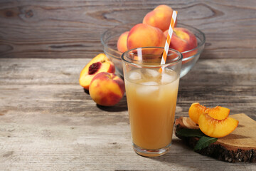 Glass of delicious peach juice with ice and fresh fruits on wooden table. Space for text
